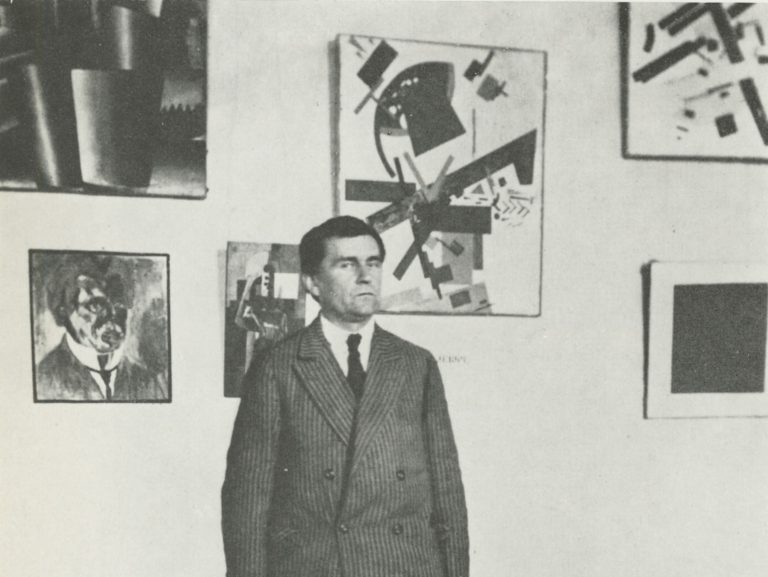 malevich suprematism: Malevich standing most probably in the Museum of Artistic Culture, St. Petersburg, Russia. 1924. Wikimedia Commons (public domain). Detail.
