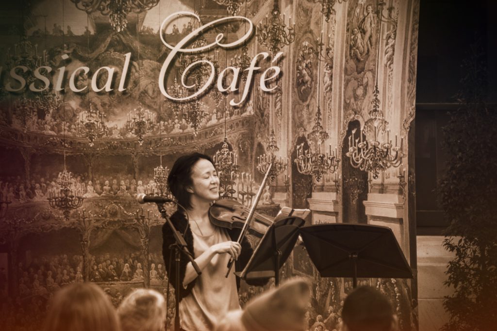 The woman plays the violin in the Cleveland Museum of Art. The words Classical Café are written in the background of the scene.