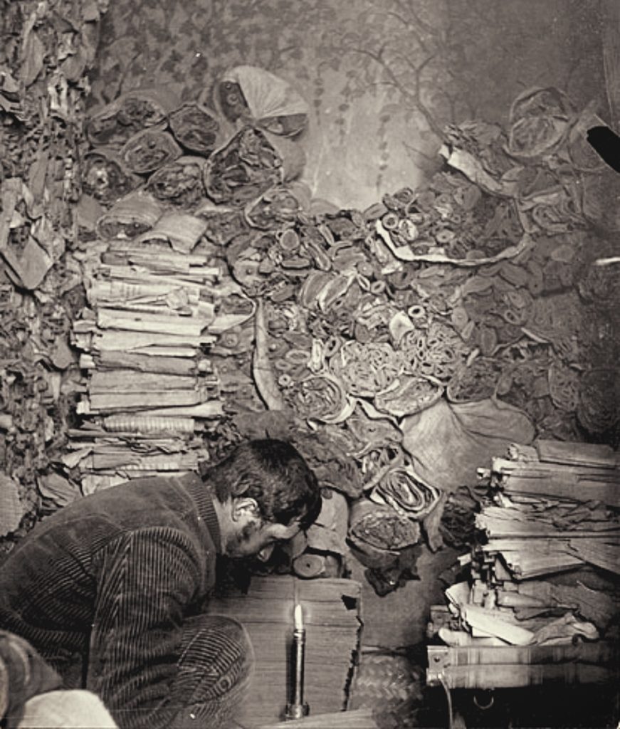 the man bending to examine manuscripts and scrolls in the dim cave