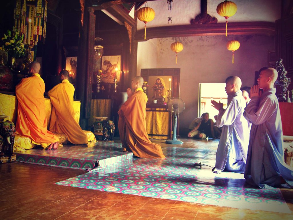 the Buddhist monks are praying the hall of the buddhist temple, figures of bodhisattvas and people watching are in the background