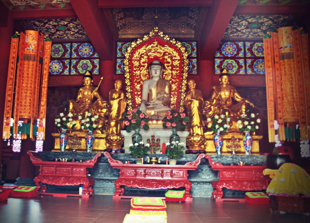sitting buddha surrounded by gilded deities in the hall of the buddhist temple