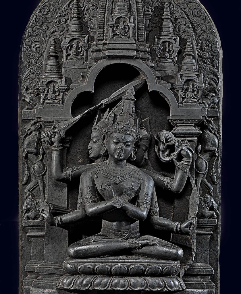 the stone sculpture of the deity Manjushri with three heads and four arms and five miniature stupas above him. Manjuvajra Mandala. 