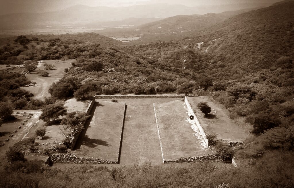 The remains of the main stone pitch for the ballgame in Mexico with the slanted platforms on both sides and view on the hills and trees