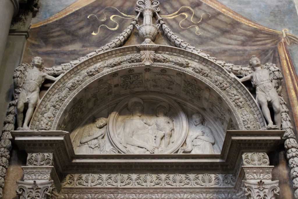 Desiderio da Settignano, Semi-circular arch with low relief tondo depicting Madonna and Child adored by two angels, Tomb of Carlo Marsuppini, Basilica of Santa Croce, Florence, Italy. 