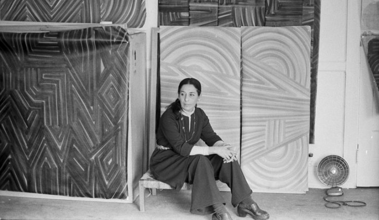 Luchita Hurtado: Luchita Hurtado, artist, photographed sitting in front of her paintings, 1970s. Photo by Matt Mulligan.
