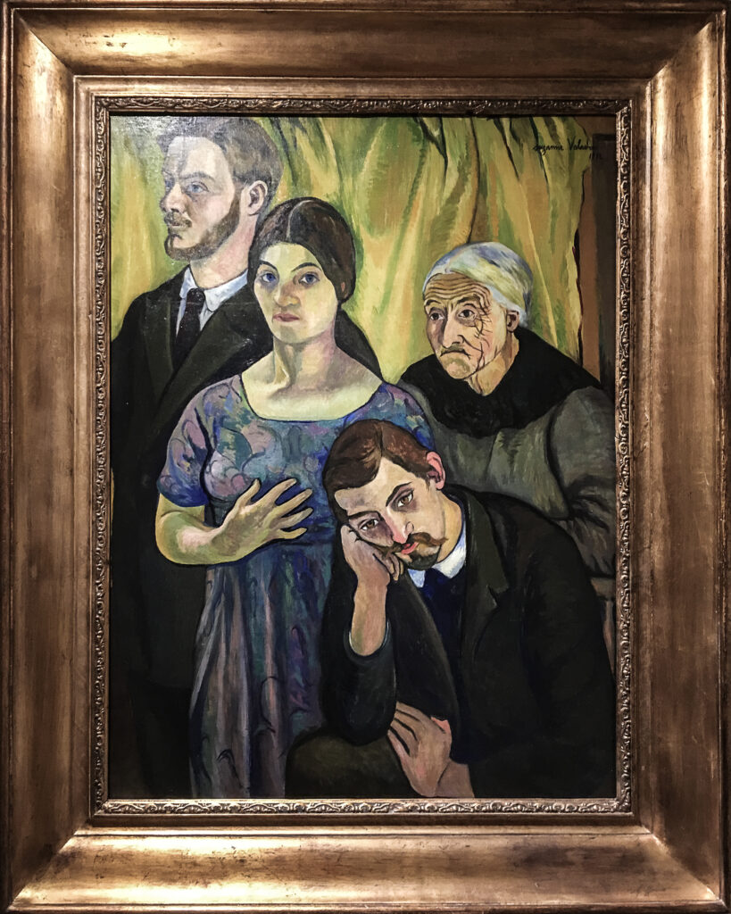 Suzanne Valadon Barnes Foundation: A family portrait with three white figures standing and white man sitting. The man sitting is hunched over with one hand on his knee and his head in his hands. The far left figure is a man facing out of the canvas, the woman next to him stands with her hand in her chest. Next to her an older woman is also standing behind the seated man.
