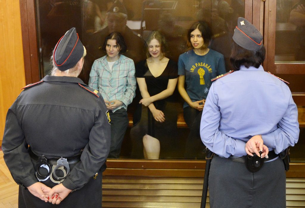 actionism in russia: Pussy Riot members sitting in a glass-walled cage during court hearing in Moscow, 2012