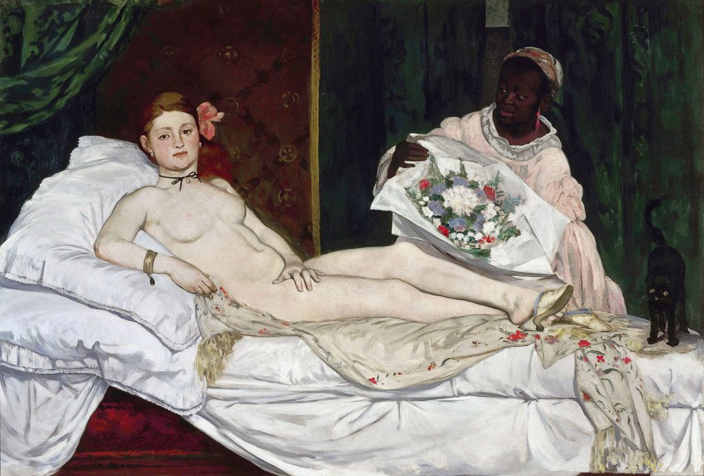 A nude Caucasian woman lays on an unmade bed, she has a choker, heels, and a flower in her hair - a frightened black cat is at her feet. A Black woman stands next to her with a bouquet of flowers.