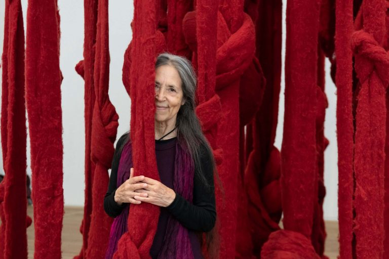 Cecilia Vicuña: Portrait of Cecilia Vicuña in front of Quipu Womb 2017 at Tate Modern, 2022. Photo by Lucy Dawkins.

