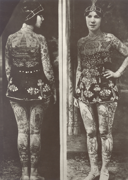 A black and white newspaper image of the front and back of young Caucasian woman. She is wearing a short dress and covered in tattoos with her hand on her hip.