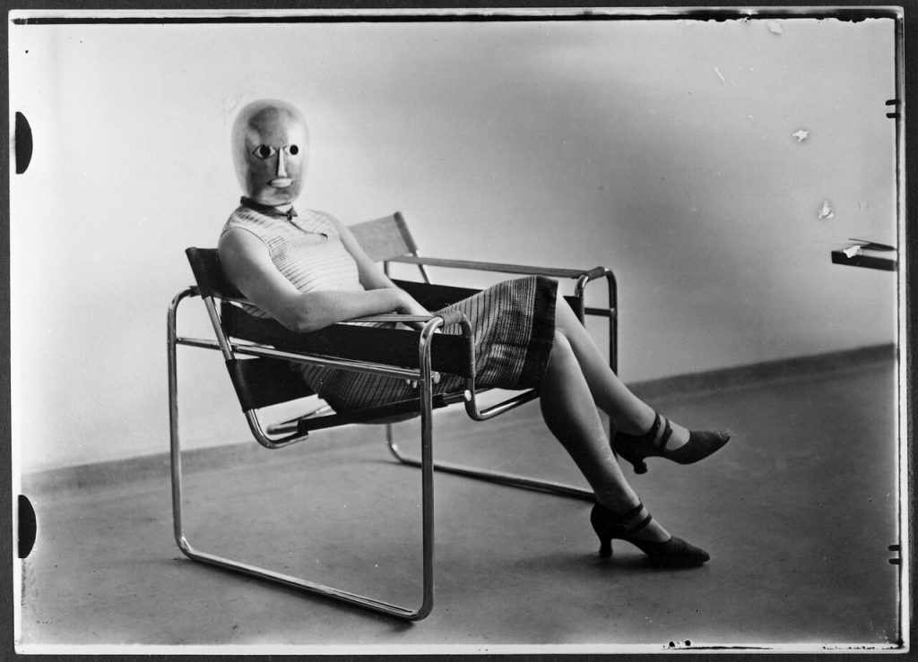 gropius biography: Woman wearing an Oskar Schlemmer mask sitting on Marcel Breuer’s Wassily Chair, ca. 1926. Photo by Erich Consemüller. Bauhaus-Archiv Berlin. © Dr. Stephan Consemüller.
