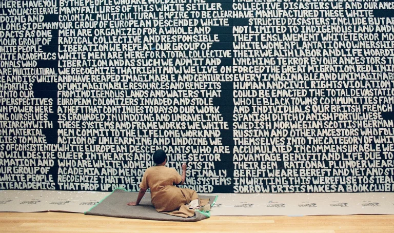 Xaviera Simmons: Xaviera Simmons working on the imposing wall of language, Crisis Makes a Book Club, Queens Museum, New York, NY, USA. Photo by Zachery K. Ali via The New York Times. Detail.
