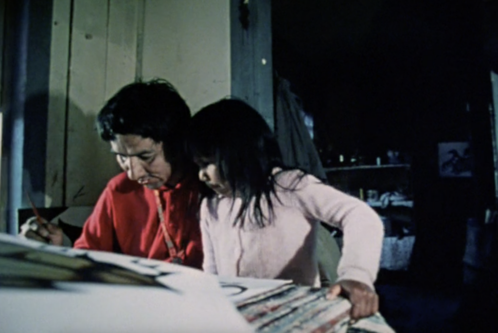 Norval Morrisseau: Film still of Norval Morrisseau painting alongside his daughter from the National Film Board documentary The Paradox of Norval Morrisseau, 1974.
