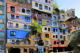 Photograph showing Hundertwasserhaus, a residential building with colorful facade and vegetation on the roof.