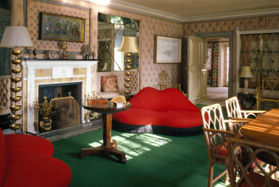Photograph showing a room with a sofa in a shape of lips among other furniture.