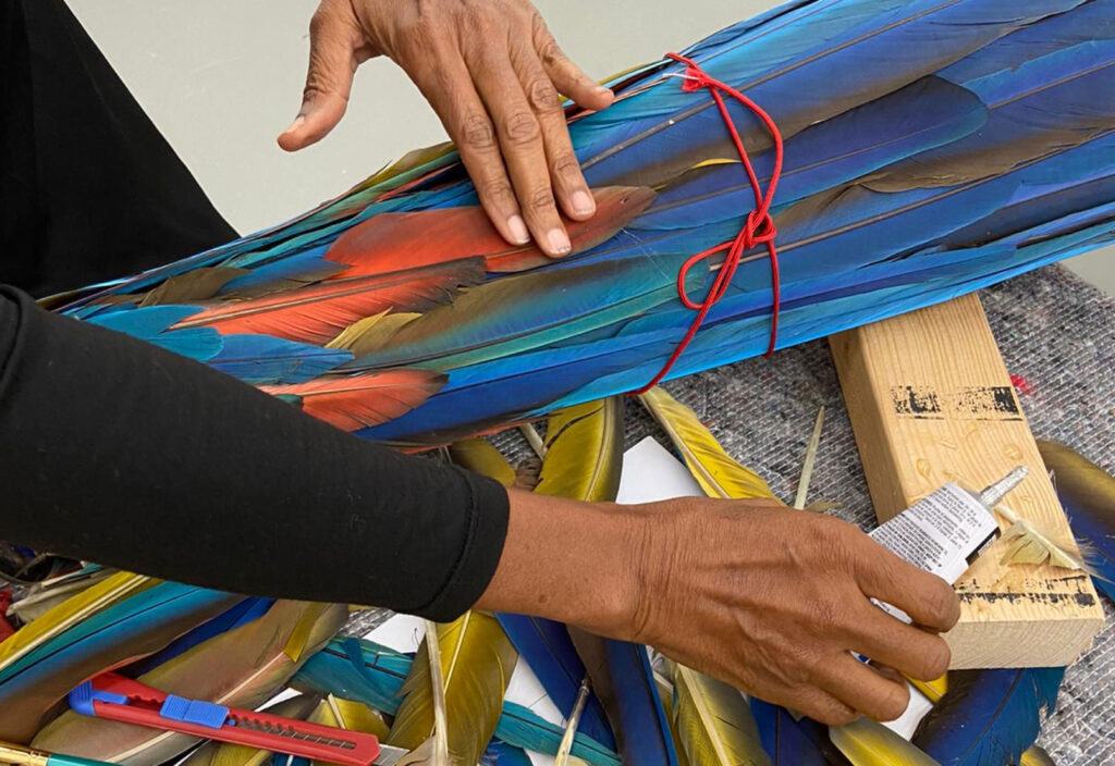 Jasmine Thomas-Girvan: Jasmine Thomas-Girvan working with macaw feathers during the creation process. Photograph by Rhonda Chan Soo.
