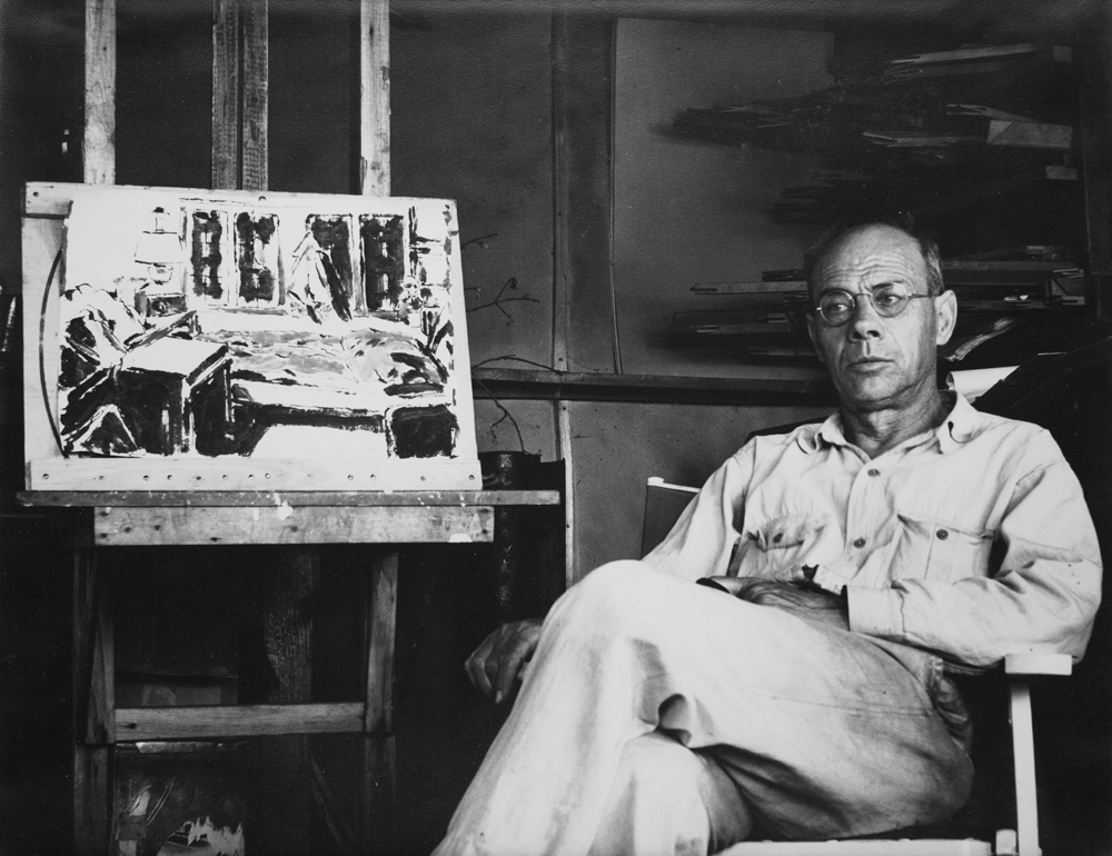 David Milne: David Milne in his cabin at Six Mile Lake with a version of Cabin Night on the easel, ca. 1938. Photograph by Douglas Duncan, Art Windsor-Essex, Windsor, Canada. Art Gallery of Sudbury.
