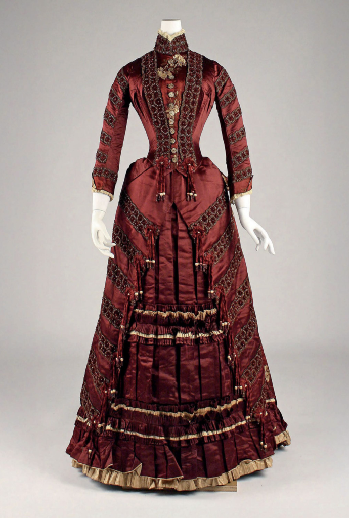 gilded age fashion: A pleated and embroidered beauty in maroon satin embellished with glass beads, 1879, Leroyer & Ducas of Paris, France. Elizabeth L. Block, Gilded Age Fashion, 2026, Hardie Grant Books, p. 19.
