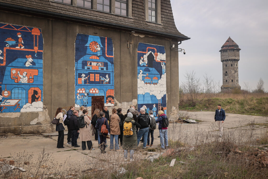upper silesia: Mural by Dajse, 2022. Group of Polish and German journalists in front of the Szopienice mural at the zinc smelter “Uthemann”, Katowice, Poland. Photo by Tomasz Kaczor, 2026.
